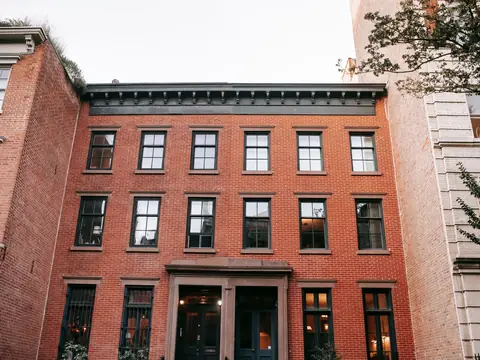 A brick townhouse with black window frames beside trees on a city street