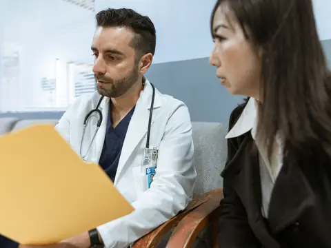 A doctor in a white coat talking with a woman in a bright room