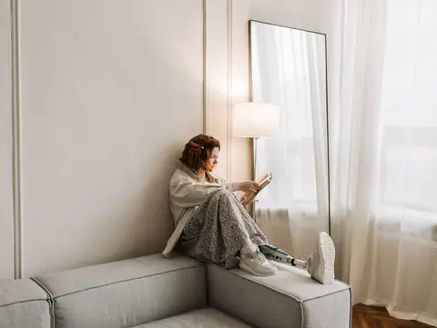 A woman reading on a window seat in a bright room with white curtains